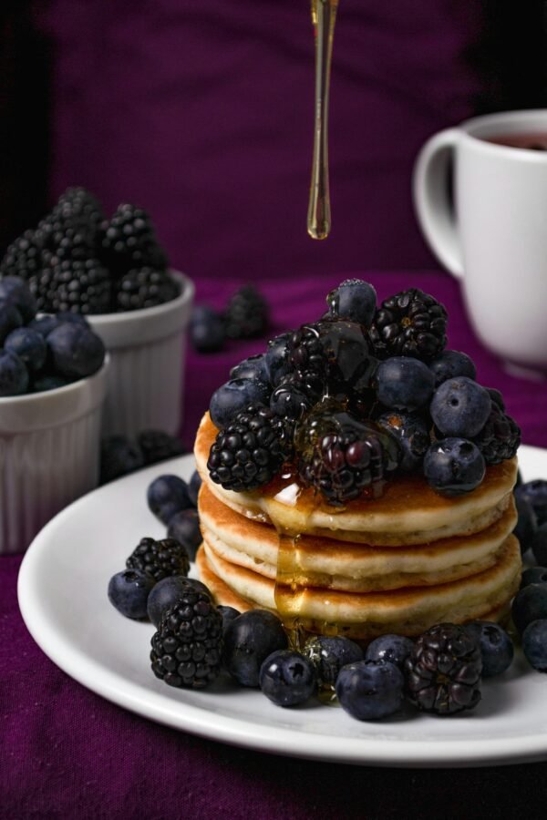 Stack of fluffy pancakes topped with fresh blackberries and blueberries, drizzled with honey, perfect for a delicious breakfast.