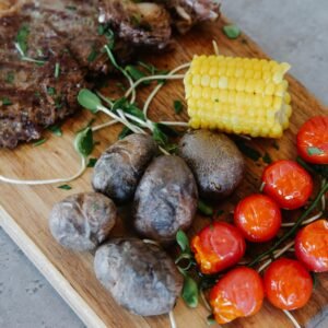 Delicious grilled steak with potatoes, tomatoes, and corn on a wooden board.