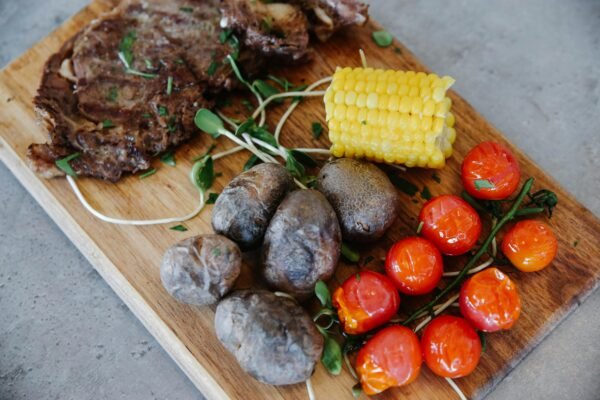 Delicious grilled steak with potatoes, tomatoes, and corn on a wooden board.